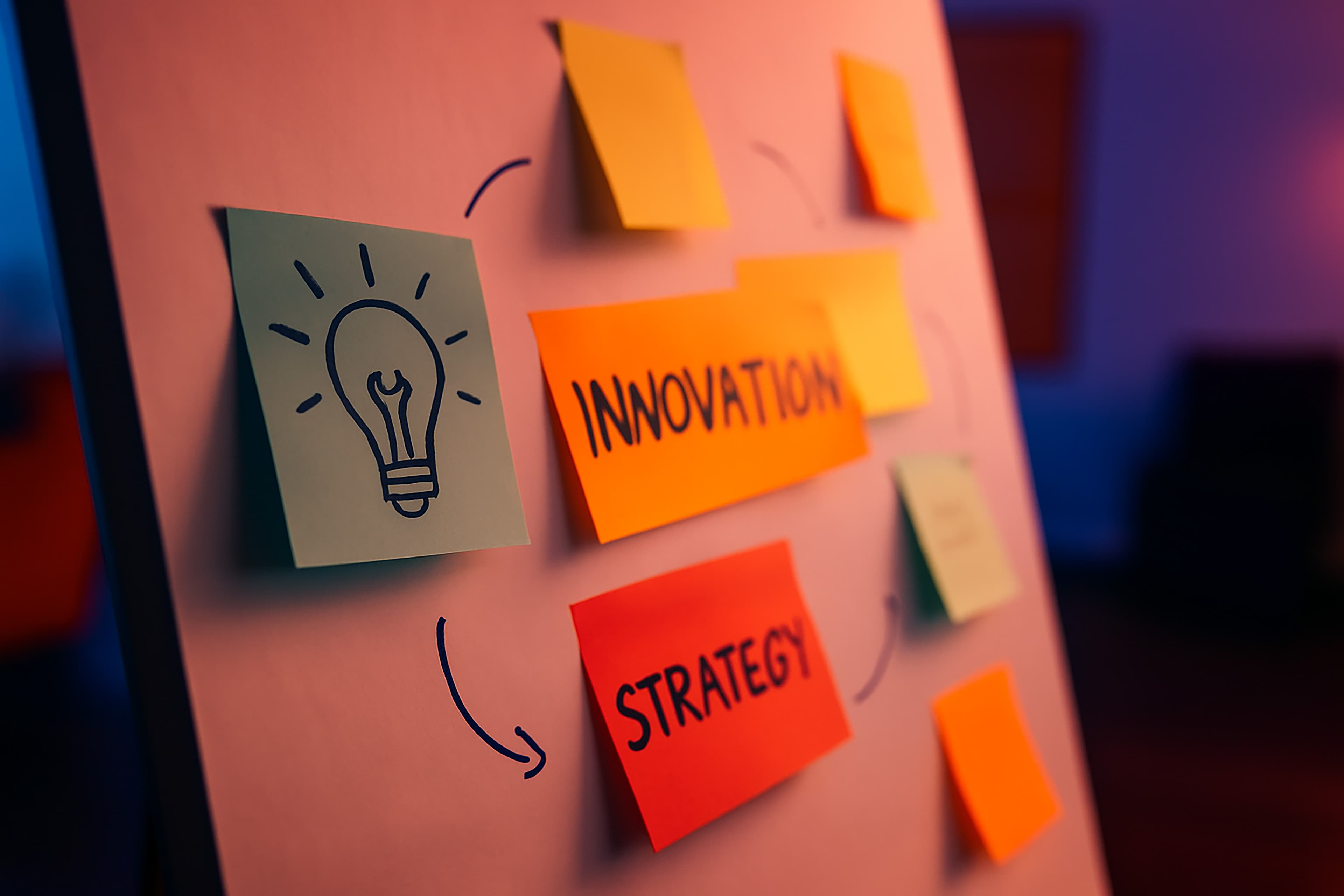 A whiteboard with colorful sticky notes, including drawings and words like INNOVATION and STRATEGY, connected by arrows, suggesting brainstorming or planning in a creative office setting.